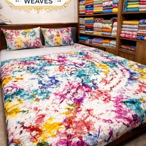 May include: A bed with a colorful, tie-dye style comforter and two matching pillowcases. The bedding features a vibrant mix of colors including pink, blue, yellow, and purple. The brand name "Khadija Weaves" is displayed above the bed.