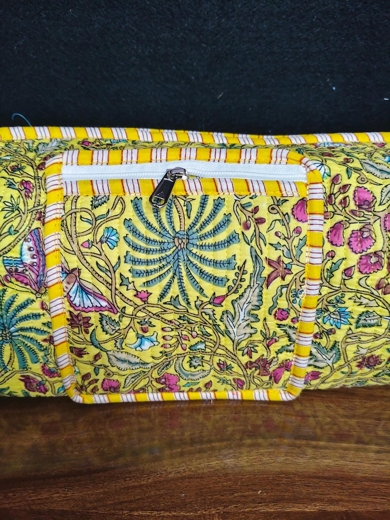 Puede incluir: Bolso amarillo con estampado floral y bolsillo con cremallera blanco. El bolso presenta un dise&ntilde;o floral colorido con detalles en rosa, azul y verde. Los bordes est&aacute;n ribeteados con tela a rayas amarillas y blancas.