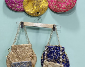 Puede incluir: Una colección de bolsos redondos bordados en varios colores, incluyendo rosa, amarillo, azul y beige. Cada bolso presenta intrincados patrones florales dorados y correas con cuentas de perlas. Los bolsos cuelgan contra una pared azul claro.