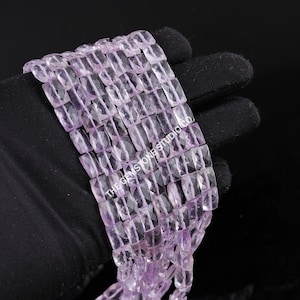 May include: Close-up of strands of light purple amethyst beads. The rectangular beads are faceted and strung together. The text "THE GEMSTONE STUDIO CO" is visible on the right side of the image.
