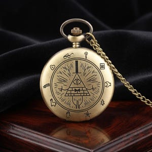 Op de afbeelding: Antieke bronzen zakhorloge met een ketting. De wijzerplaat toont een gedetailleerde illustratie van een alziend oog in een driehoek, omringd door verschillende symbolen. Het horloge heeft een ronde vorm en een getextureerde afwerking.