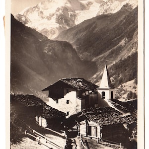 Puede incluir: Postal vintage en blanco y negro con un paisaje de montaña y un pueblo. La imagen muestra una iglesia con un alto campanario y varios edificios con tejados oscuros y texturizados. El texto "1916 La Sage et Pigne d'Arolla" es visible.