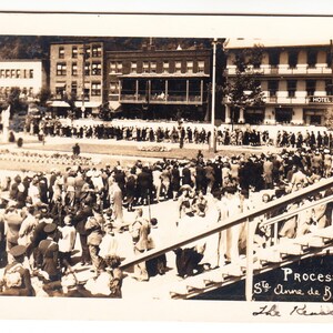 May include: Vintage black and white photograph of a large crowd gathered in front of buildings, likely a parade or procession. The image includes the text "Procession Ste Anne de Beaupre" and the date "1913".