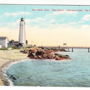 May include: A vintage postcard depicting the Old Lighthouse at Light-house Point in New Haven, Connecticut. The image shows a tall, white lighthouse, a pier, and a beach with calm water under a blue sky. Text on the card reads "New Haven, Conn. (East Haven) Light-house Point. The Old Light-house."