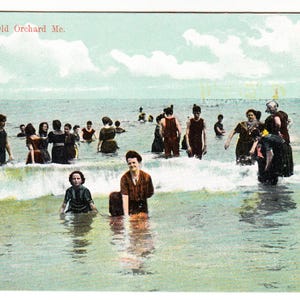 Puede incluir: Postal vintage titulada "Bath Scene, Old Orchard Me." que representa a un grupo de personas en el océano. La imagen muestra a personas con trajes de baño vintage, de pie en el agua, con olas en primer plano y un cielo azul claro.