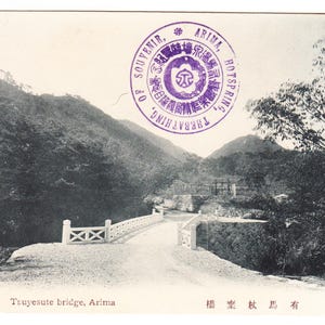 May include: Vintage black and white postcard depicting Truyesute bridge in Arima, Japan. The image shows a bridge over a road with mountains and trees in the background. A purple stamp is visible.