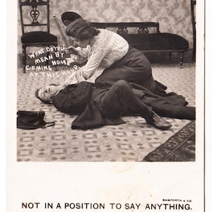 May include: Vintage black and white postcard featuring a woman leaning over a man lying on the floor. Text on the card reads "WHAT DO YOU MEAN BY COMING HOME AT THIS HOUR" and "NOT IN A POSITION TO SAY ANYTHING."