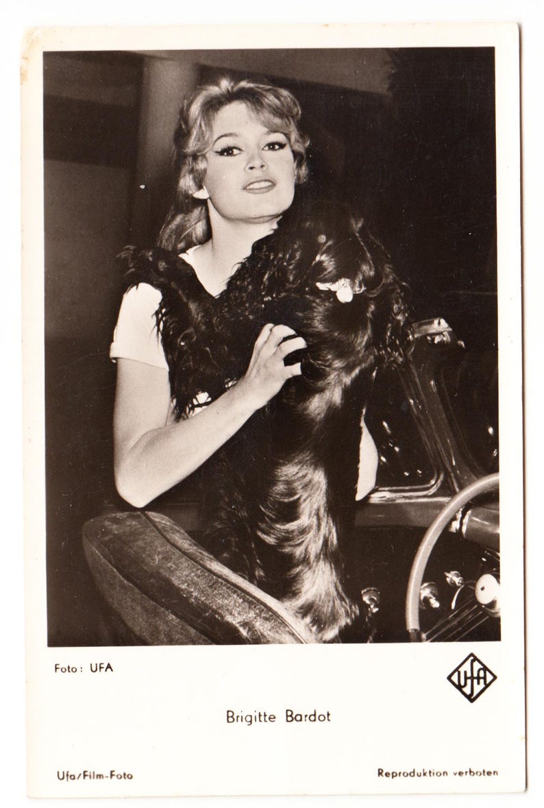 May include: A white ceramic mug with a black handle and the text "But First, Coffee" in a bold, black font. The mug is set against a blurred background, suggesting a cosy setting.