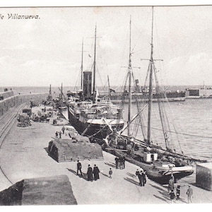 Op de afbeelding: Vintage zwart-wit ansichtkaart met de haven van Melilla, met de tekst "Melilla. Muelle Villanueva." Verschillende schepen liggen aangemeerd aan de pier, met zichtbare mensen en vracht. De scène legt een historische maritieme omgeving vast.