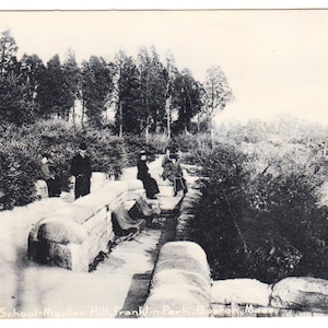May include: Vintage black and white postcard featuring a scenic view of Terrace, School-Master Hill, Franklin Park, Boston, Mass. The image shows a stone pathway with people, trees, and a field in the background. The postcard is a historical item.