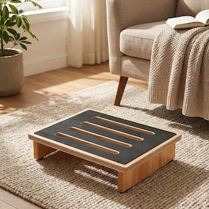 May include: A wooden footstool with a black, textured top and four rectangular cutouts. The footstool is made of light-colored wood and is rectangular in shape. It is placed on a beige rug in a living room setting.
