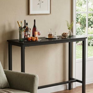 May include: A black, rectangular bar table with a variety of bottles, glasses, and fruit on top. A framed botanical print hangs on the wall above the table. The table is in a living room setting.