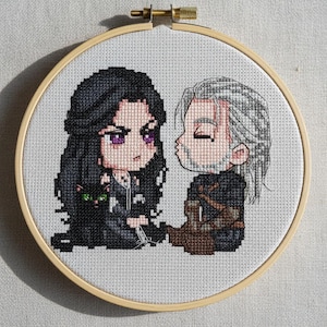 May include: Cross-stitch embroidery in a wooden hoop features two chibi-style figures, a woman with black hair and a cat, and a man with white hair. The figures are kissing. The background is a light gray fabric.