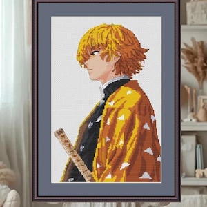 May include: Framed cross-stitch art featuring a side profile of an anime character with spiky yellow hair and a yellow and brown patterned robe. The character is holding a sword. The artwork is in a dark brown frame.
