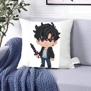 May include: White square pillow featuring a pixelated anime-style character with black hair, blue eyes, and a black jacket, holding a sword. The pillow is on a gray couch with a blue blanket.