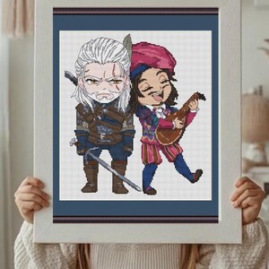 May include: Cross-stitch art featuring two characters from The Witcher series. One character has white hair and a sword, the other plays a lute and wears a pink hat. The artwork is framed in a white rectangular frame.
