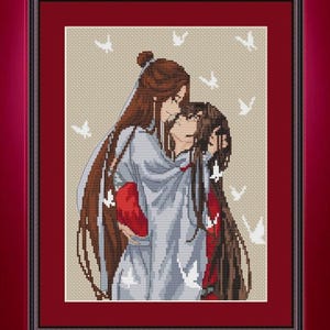 May include: Cross-stitch artwork depicting two figures in an embrace, with long brown hair and robes. White bird motifs are scattered on a beige background. The artwork is framed in a dark red frame, set against a red background.