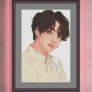 May include: Framed cross-stitch portrait of a person with brown hair and a light yellow shirt. The artwork is set against a gray background within a black frame, surrounded by a pink neon border.