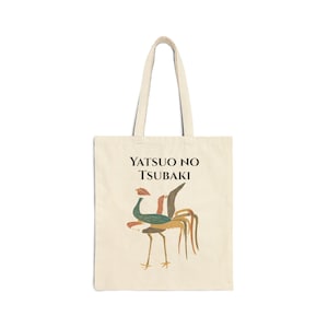 May include: Cream-colored tote bag with a colorful bird illustration and the text "YATSUO NO TSUBAKI" in black. The bird design features green, red, brown, and gold accents. The bag has two cream-colored handles.