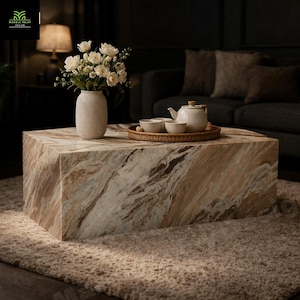 May include: A large, square marble coffee table with a beige and brown veined pattern. A white vase with white flowers sits on the table, along with a tea set on a woven tray. The table is in a living room setting.