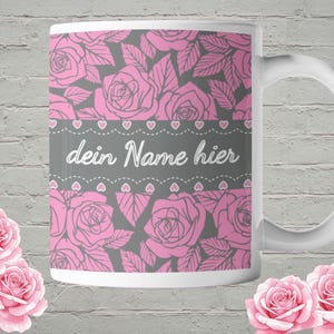 Könnte beinhalten: Weiße Keramik-Tasse mit einem floralen Rosen-Design in Rosa und Grau. Die Tasse zeigt den Text "dein Name hier" auf einem grauen Band mit Herz-Akzenten. Rosa Rosen sind um die Tasse angeordnet.