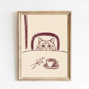 Könnte beinhalten: Ein gerahmter Druck mit einer Katze, die über einen Tisch schaut. Die Katze ist in einem einfachen Strichstil gezeichnet. Eine Tasse Kaffee und ein Zweig Blätter befinden sich auf dem Tisch. Die Farbpalette ist neutral mit Braun- und Beigetönen.