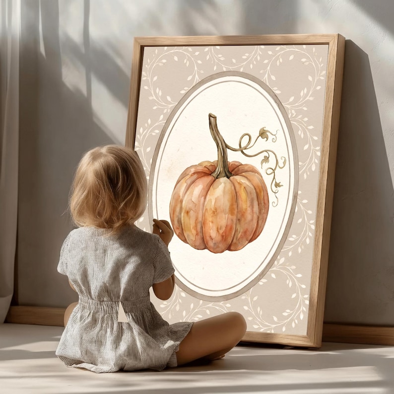 Puede incluir: Una l&aacute;mina de arte enmarcada que presenta una ilustraci&oacute;n en acuarela de una calabaza naranja con tallo verde y zarcillos, centrada dentro de un borde ovalado sobre un fondo beige claro decorado con delicados patrones de enredaderas blancas.