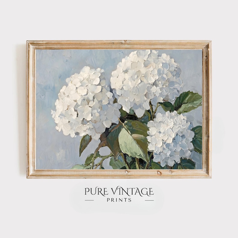 Puede incluir: Pintura enmarcada de hortensias blancas con hojas verdes sobre un fondo azul claro. La obra de arte tiene un estilo impresionista texturizado. El marco es de color madera clara. El texto "PURE VINTAGE PRINTS" est&aacute; en la parte inferior.