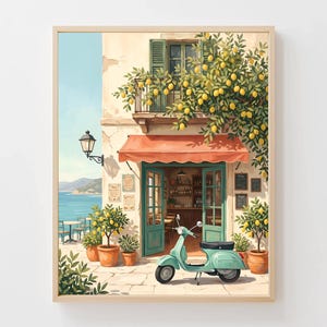 Op de afbeelding: Een ingelijste prent van een charmante Italiaanse caféscène. Het kunstwerk toont een gebouw met een rode luifel, groene luiken en een balkon vol citroenen. Een turquoise scooter staat voor het café geparkeerd en potcitroenbomen flankeren de ingang.