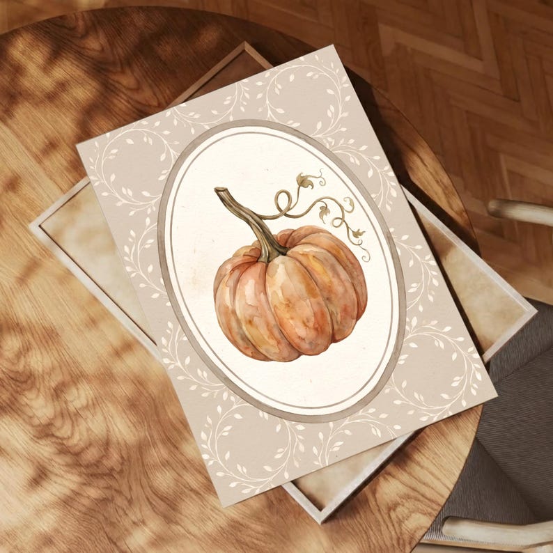 Puede incluir: Una impresi&oacute;n rectangular que presenta una ilustraci&oacute;n en acuarela de una calabaza naranja con un tallo verde y zarcillos. La calabaza est&aacute; centrada dentro de un marco ovalado sobre un fondo beige claro decorado con un patr&oacute;n de hojas blancas.