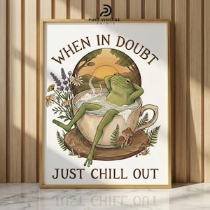 May include: A framed print with the text "WHEN IN DOUBT JUST CHILL OUT". The artwork features a green frog relaxing in a teacup, with a sunset and floral elements in the background. The print is in a gold frame.