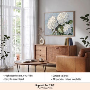 Puede incluir: Una impresi&oacute;n floral enmarcada con flores de hortensias blancas sobre un fondo azul claro. La obra de arte se exhibe sobre un mueble de madera con una puerta tejida. La imagen tambi&eacute;n muestra una mesa de centro, un sill&oacute;n de cuero y texto que dice "Archivos JPG de alta resoluci&oacute;n" y "F&aacute;cil de descargar".