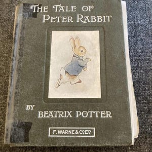 以下が含まれることがあります： ピーターラビットの物語、ビアトリクス・ポター著のヴィンテージ本。表紙は緑色で、タイトルと著者の名前が白で書かれています。イラストには青いジャケットを着たウサギが描かれています。出版社はF. Warne & Co.