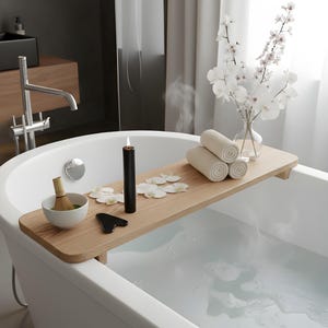 May include: A modern bathroom scene with a white bathtub filled with water. A wooden bath tray holds a black candle, a bowl with a whisk, a black gua sha tool, and rolled towels. White flower petals and a vase of white flowers add to the spa-like ambiance.