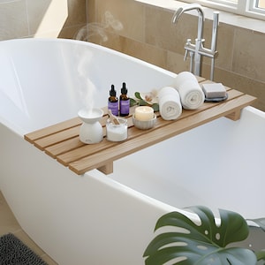 Puede incluir: Una bandeja de baño de madera cruza una bañera blanca, con elementos de spa. Incluye toallas blancas enrolladas, una vela encendida, botellas de aceites esenciales, un pequeño difusor de vapor y una pastilla de jabón, evocando relajación.