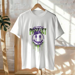 Puede incluir: Camiseta blanca con un diseño gráfico que presenta una carita sonriente con una corona, con las palabras "Glitch Protect". El diseño incorpora colores morados y verdes con un efecto de pintura goteando.
