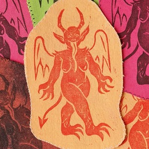 Op de afbeelding: Stoffen patches met een rood duivelsfiguurontwerp op een oranje achtergrond. De afbeelding toont andere patches in roze, groen en bordeauxrood met vergelijkbare ontwerpen. De patches hebben een gestikte rand.