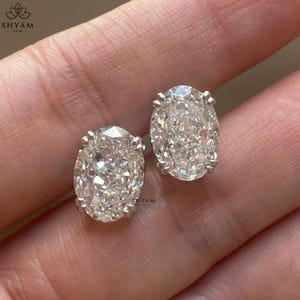 Könnte beinhalten: Ein Paar Ohrstecker mit ovalem Schliff und klaren, facettierten Steinen in silberfarbenen Metallfassungen. Jeder Ohrring weist eine brillante, facettierte Oberfläche auf, die das Licht reflektiert und die ovale Form betont.