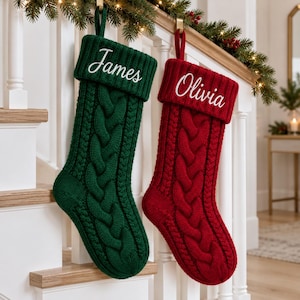 Può includere: Due calze natalizie in maglia, una verde scuro e una rossa, con motivo a trecce e bordo a coste. La calza verde è ricamata con il nome James in corsivo bianco, mentre la calza rossa presenta il nome Olivia in bianco.