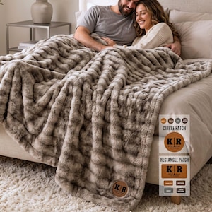 May include: A plush, textured faux fur throw blanket in shades of taupe and cream, featuring a circular leather patch embossed with the initials KR, the names Katie and Ryan, and the date 10.10.2024, with a side chart showing patch options.