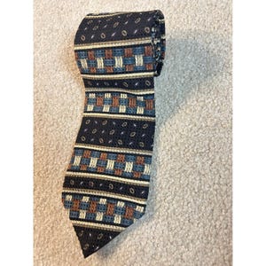 May include: A necktie featuring a dark navy blue base with a repeating pattern of small white ovals. The design includes horizontal bands of a woven basket-weave texture in shades of light blue, tan, and brown, separated by thin stripes.