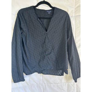 May include: Black long-sleeve blouse with a wrap-style front and a textured dot pattern. The blouse is hanging on a black hanger. The Tommy Hilfiger logo is visible on the label.