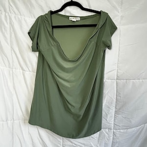 May include: Olive green short-sleeve top with a cowl neck and a hood. The top is hanging on a black hanger against a white background. The brand name "eye candy" is visible on the tag.