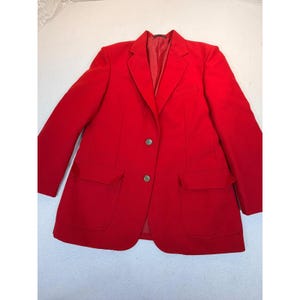 May include: A vibrant red blazer featuring a notched lapel, two front buttons, and two large flap pockets. The jacket is fully lined with matching red fabric and includes long sleeves with a structured shoulder design and a classic tailored fit.