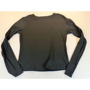 May include: A solid black long-sleeve shirt featuring a simple crew neckline and a straight hemline. The garment is constructed from a smooth, opaque fabric and is presented in a flat, unfolded position to display the full sleeve length.