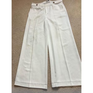 May include: Off-white wide-leg trousers featuring a high-waisted design with a button closure at the waistband, a front zipper fly, side pockets, and visible dark stitching along the seams and hemline, creating a structured and tailored appearance.