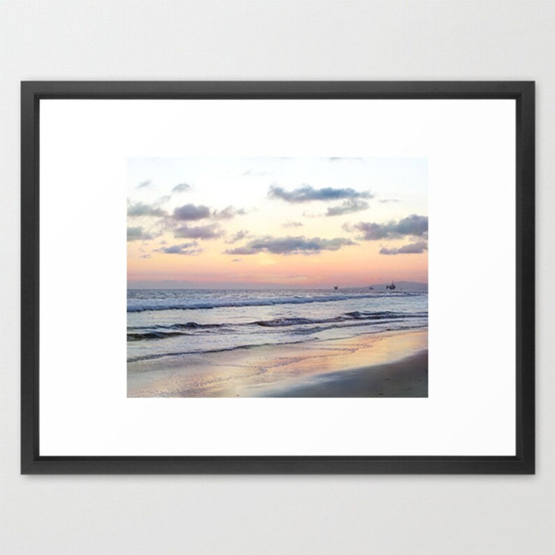 May include: A scenic photograph of a beach at sunset. The sky is a soft blend of pink, orange, and purple, with fluffy white clouds. The ocean waves are gently rolling in, creating a tranquil scene.