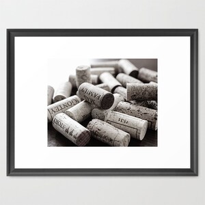 May include: A collection of wine corks in varying sizes and textures, with visible text from the wine bottles. The corks are in shades of brown and beige, creating a monochromatic image. Some corks have visible text such as "MAS FAMILY" and "STORY".