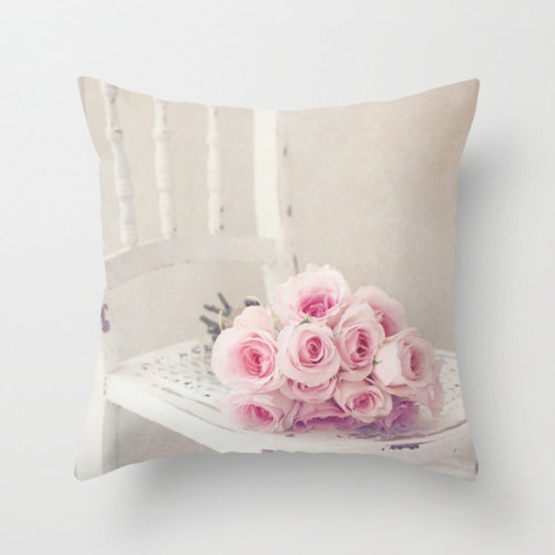 K&ouml;nnte beinhalten: Ein Strau&szlig; hellrosa Rosen liegt auf einem wei&szlig;en, abgenutzten Stuhl. Die Rosen sind locker und nat&uuml;rlich angeordnet, und der Stuhl ist ein schlichtes, klassisches Design.