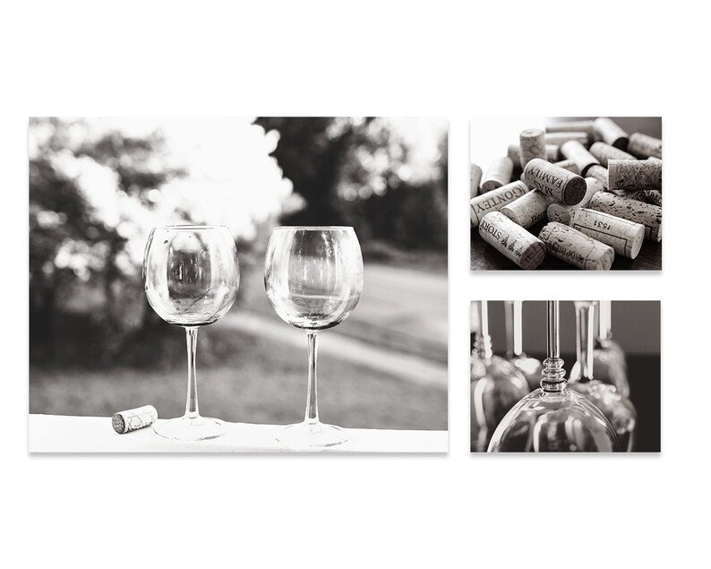 May include: Two clear glass wine glasses on a white surface with a cork on the left side of the image. The glasses are empty and have a round bowl and a long stem. The background is out of focus and shows a blurred image of trees and a grassy area.
